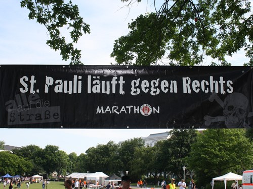 Ein Banner hängt unter Bäumen. Darauf steht: St. Pauli läuft gegen Rechts.